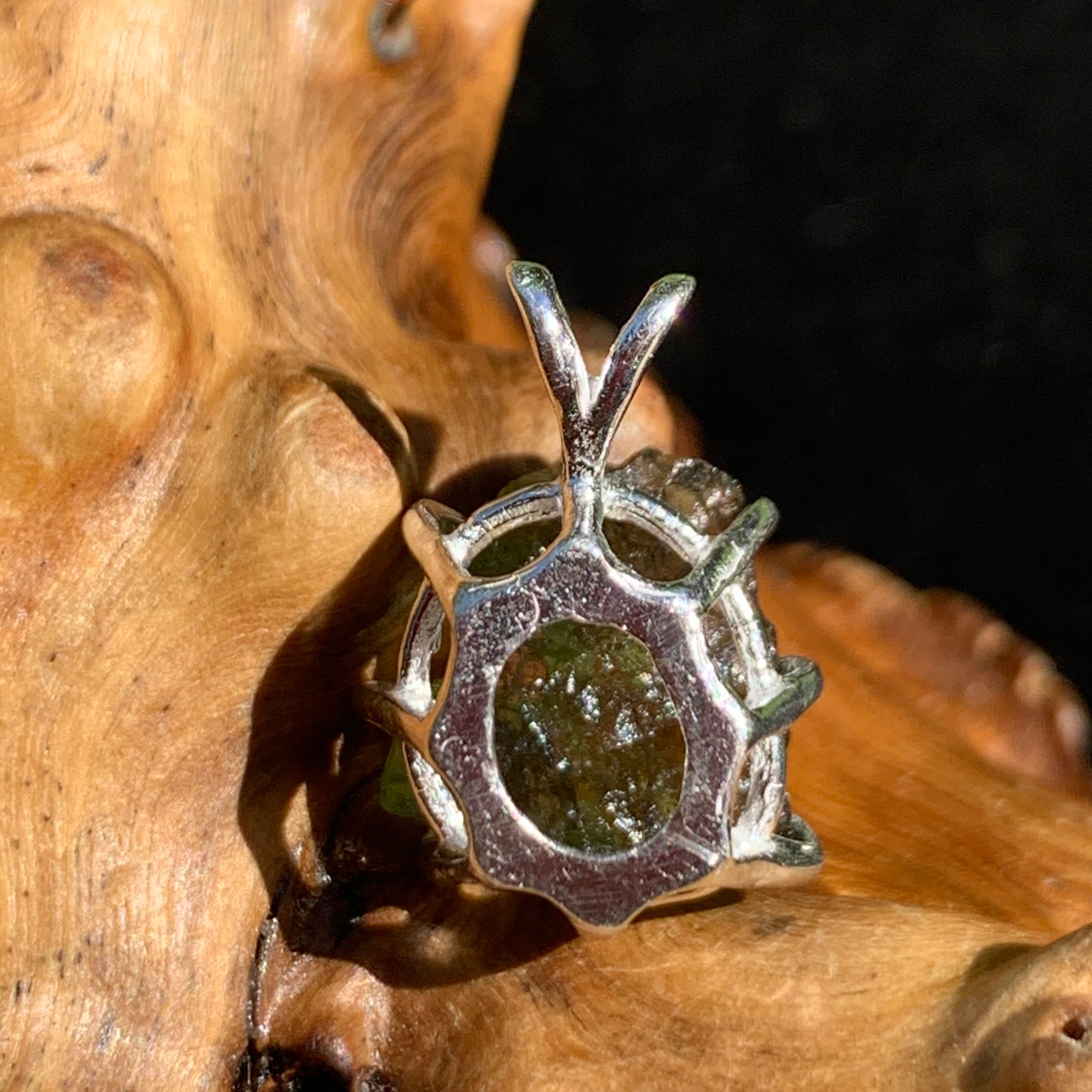 backside of a raw moldavite tektite sterling silver basket pendant sitting on driftwood for display