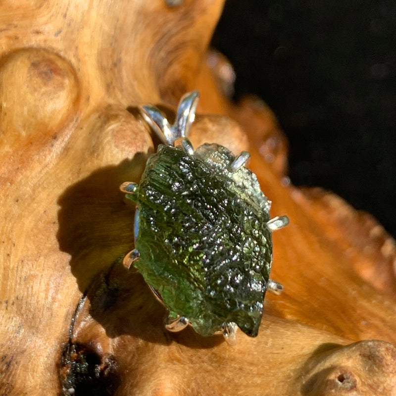 raw moldavite tektite sterling silver basket pendant sitting on driftwood for display