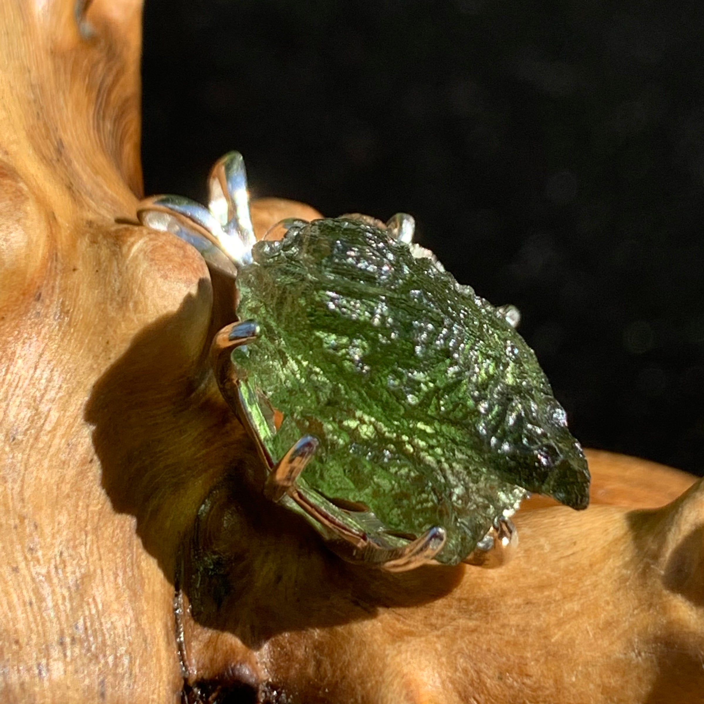 raw moldavite tektite sterling silver basket pendant sitting on driftwood for display