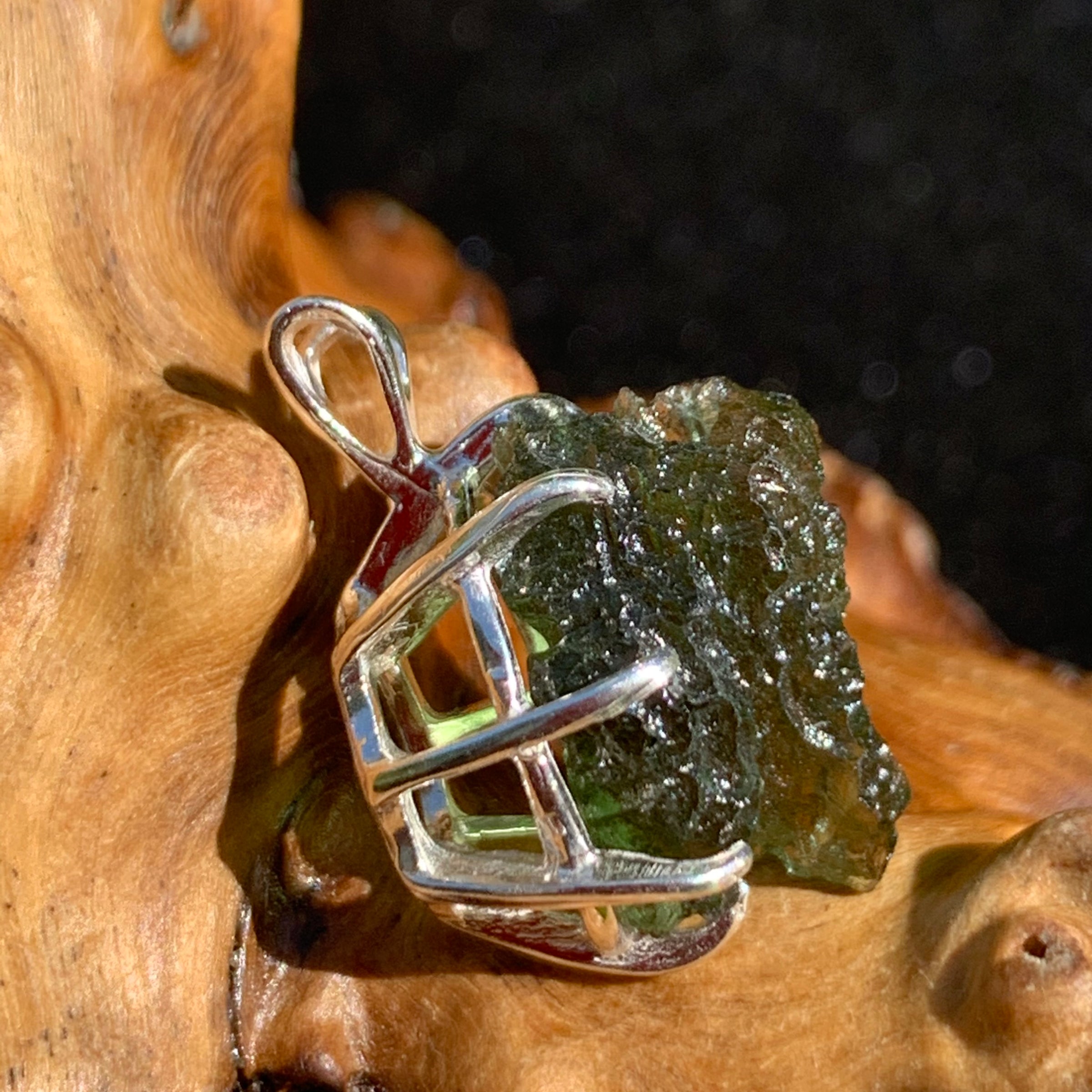 raw moldavite tektite sterling silver basket pendant sitting on driftwood for display