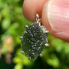 raw moldavite tektite sterling silver basket pendant held up on display to show details