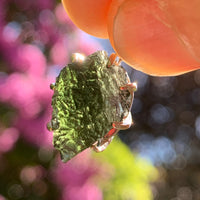 raw moldavite tektite sterling silver basket pendant held up on display with sunlight shining through to show details