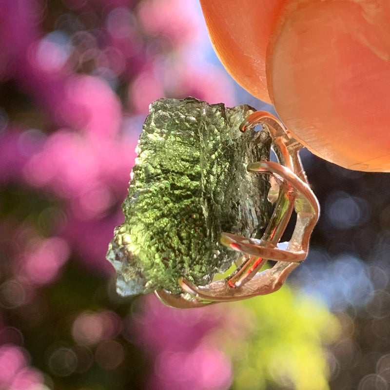 raw moldavite tektite sterling silver basket pendant held up on display with sunlight shining through to show details