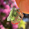 raw moldavite tektite sterling silver basket pendant held up on display with sunlight shining through to show details