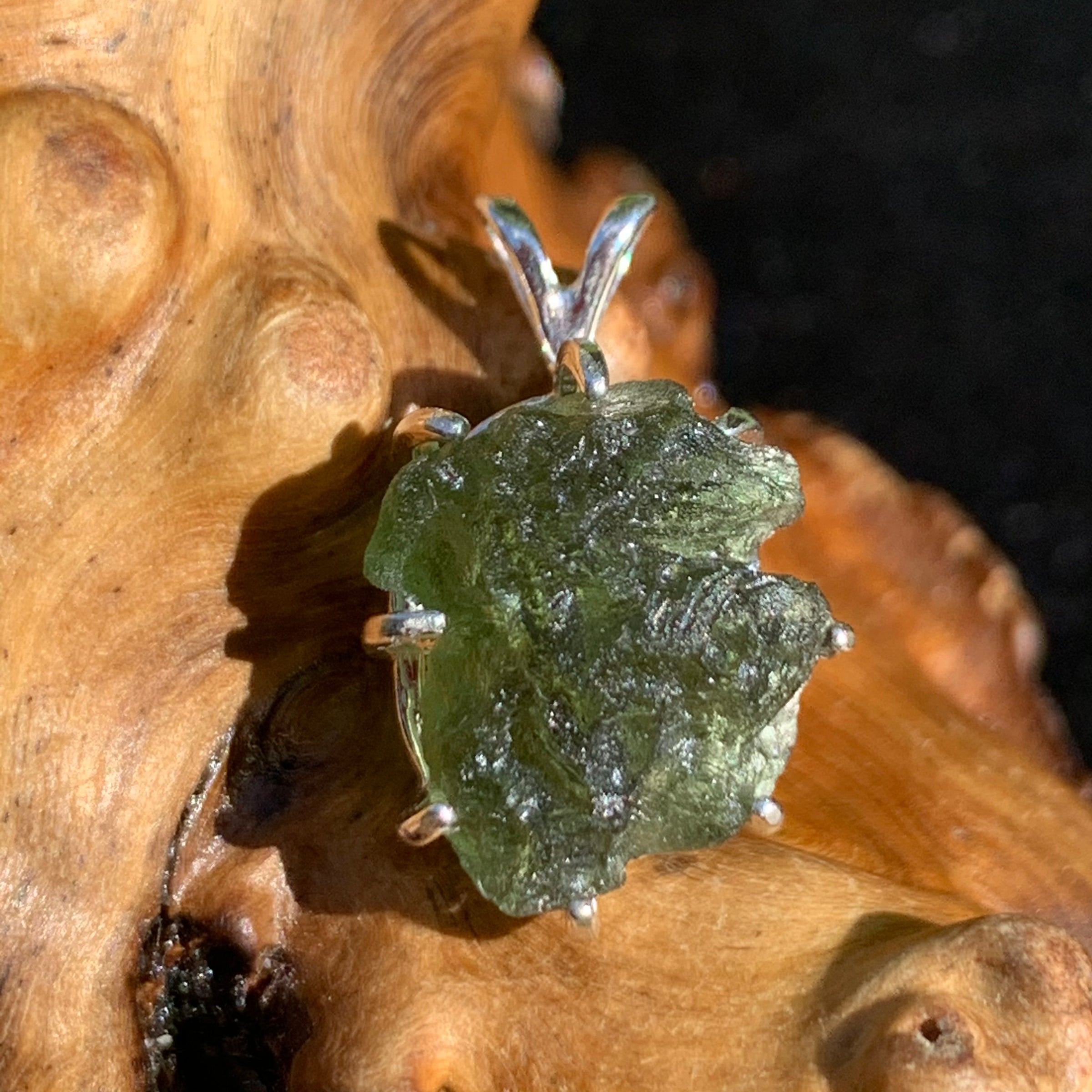 raw moldavite tektite sterling silver basket pendant sitting on driftwood for display