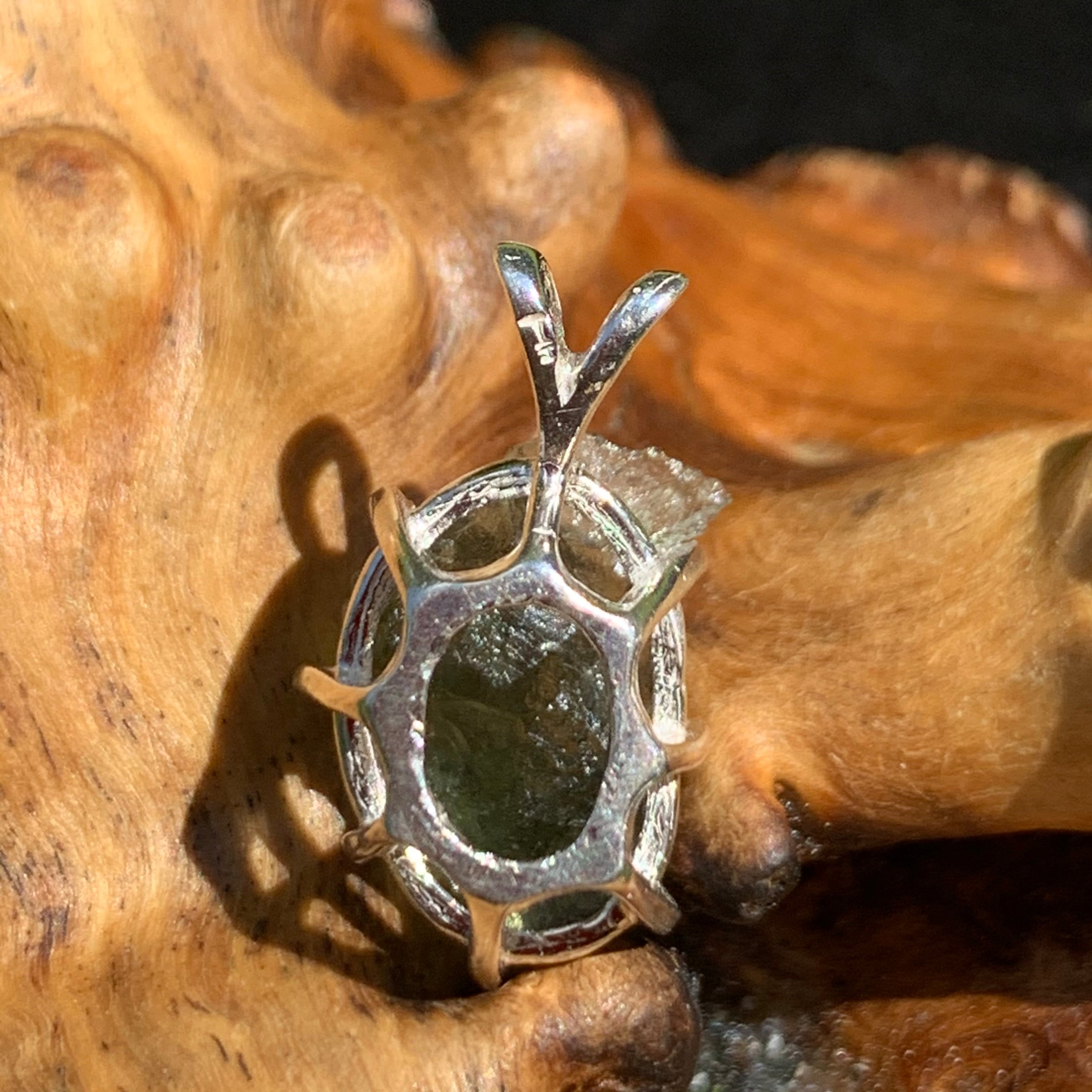 backside of a raw moldavite tektite sterling silver basket pendant sitting on driftwood for display