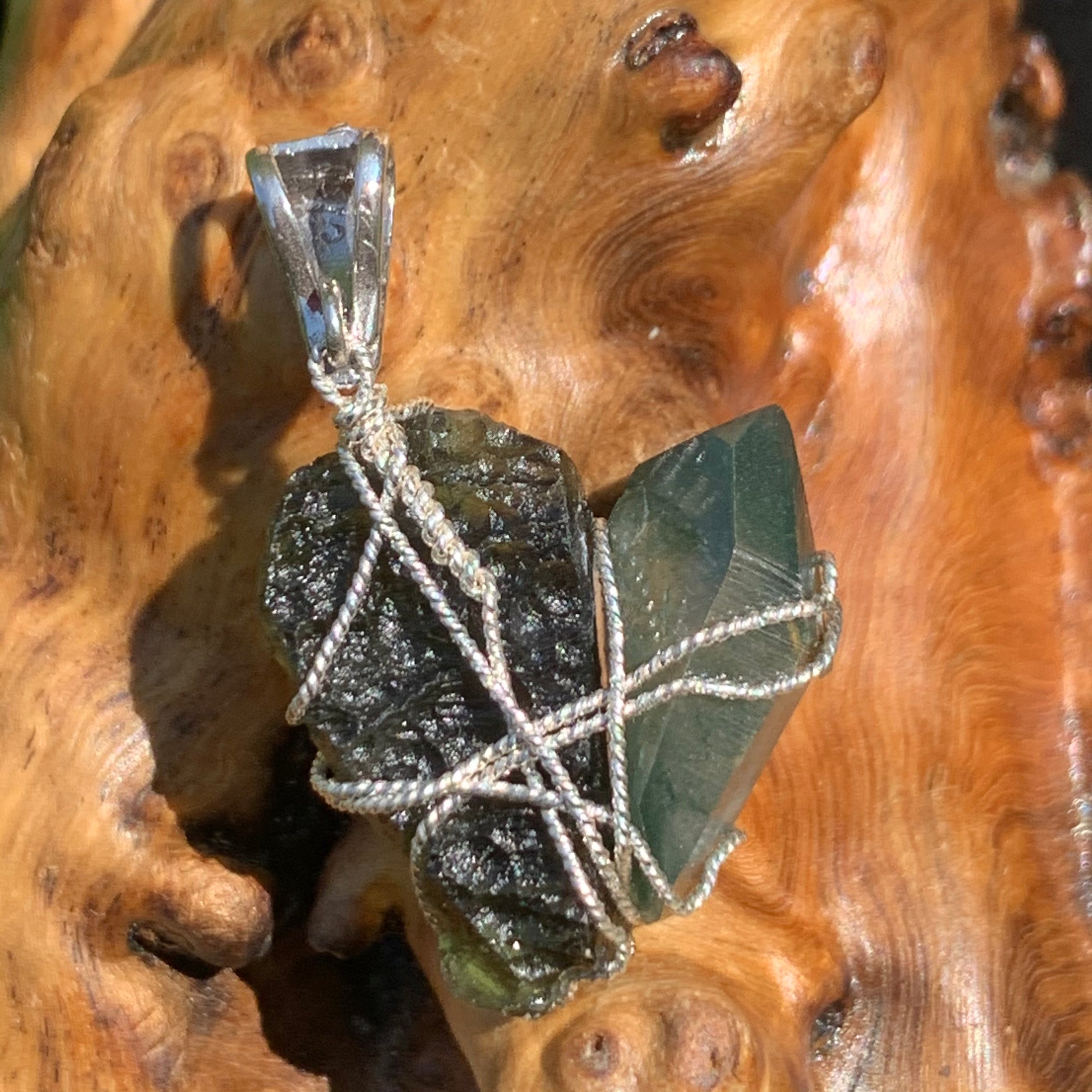 backside of a raw moldavite tektite and chlorite quartz crystal sterling silver wire wrapped pendant sitting on driftwood for display