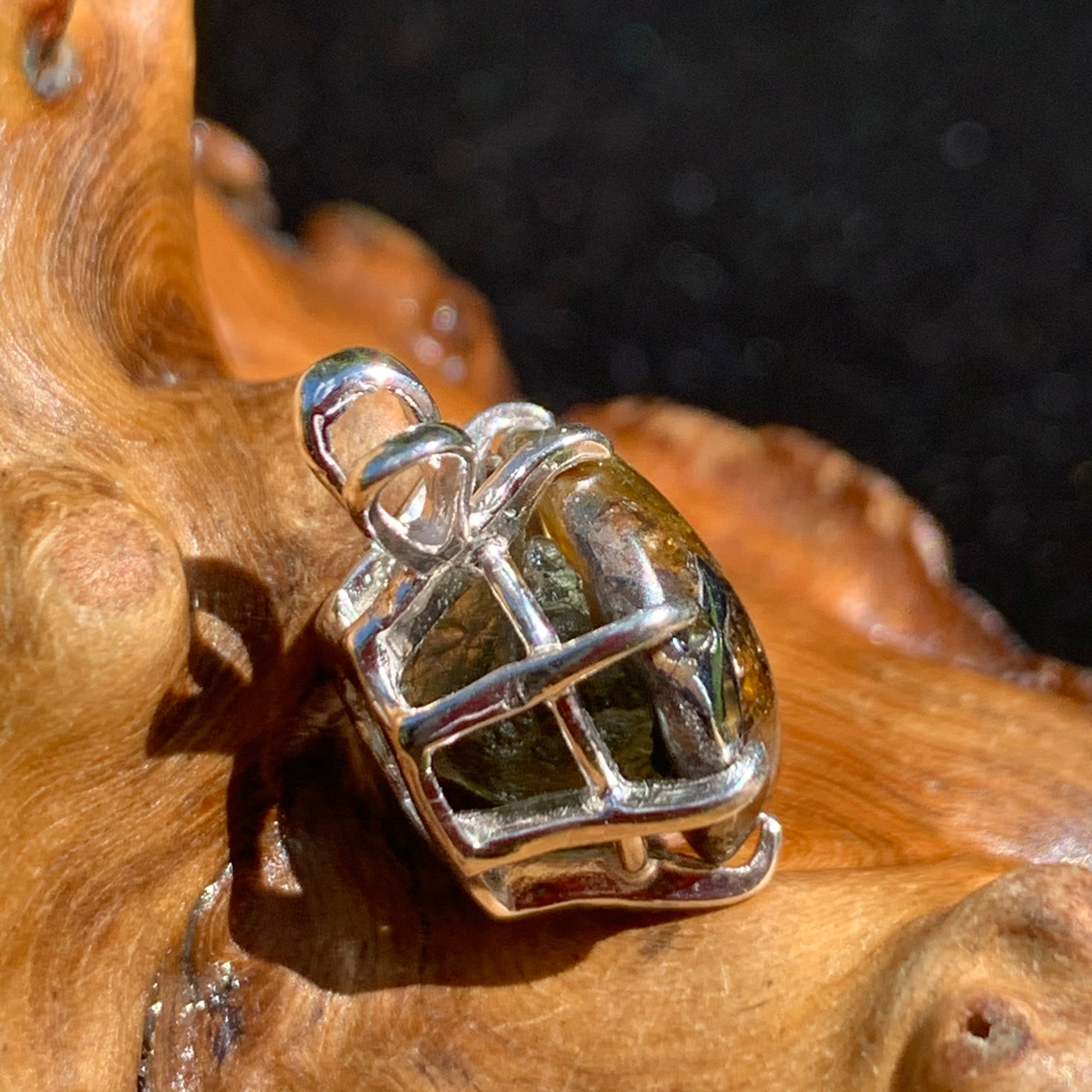 sterling silver sericho pallasite meteorite and raw moldavite tektite basket pendant sitting on driftwood for display