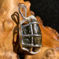 side view of a sterling silver sericho pallasite meteorite and raw moldavite tektite basket pendant sitting on driftwood for display