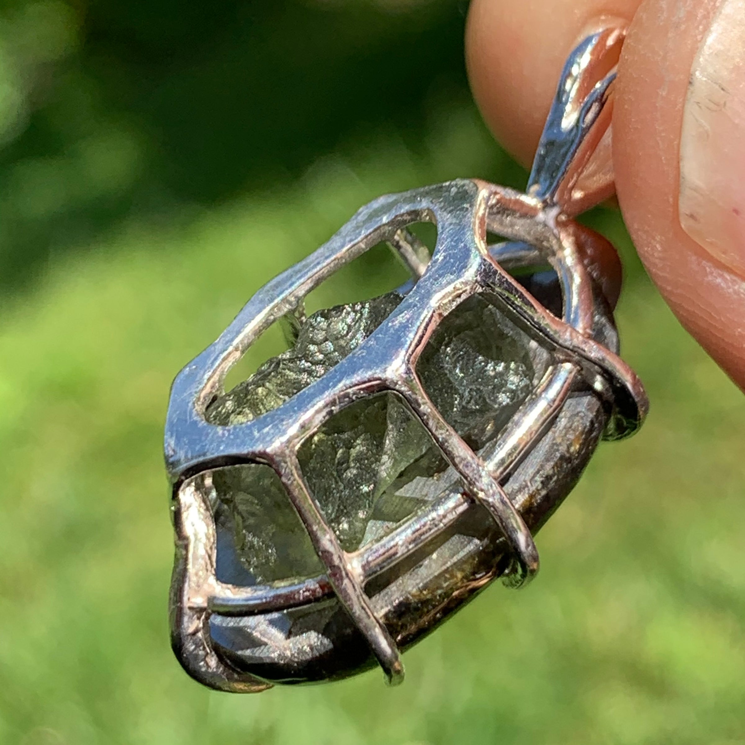 moldavite shows through the backside of a sterling silver sericho pallasite meteorite and raw moldavite tektite basket pendant held up on display to show details