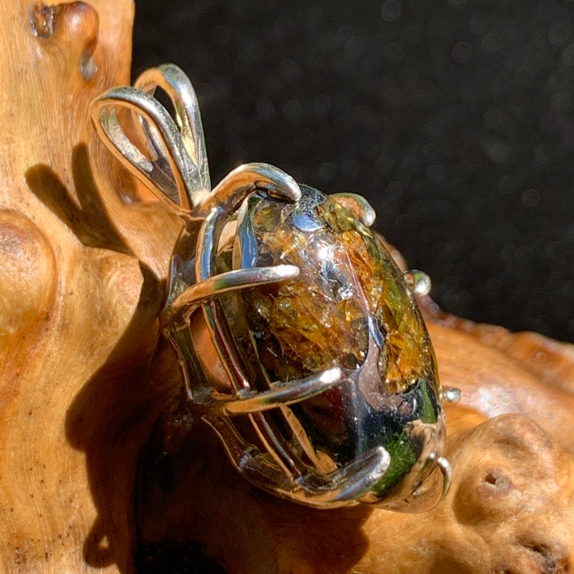 sterling silver sericho pallasite meteorite and raw moldavite tektite basket pendant sitting on driftwood for display