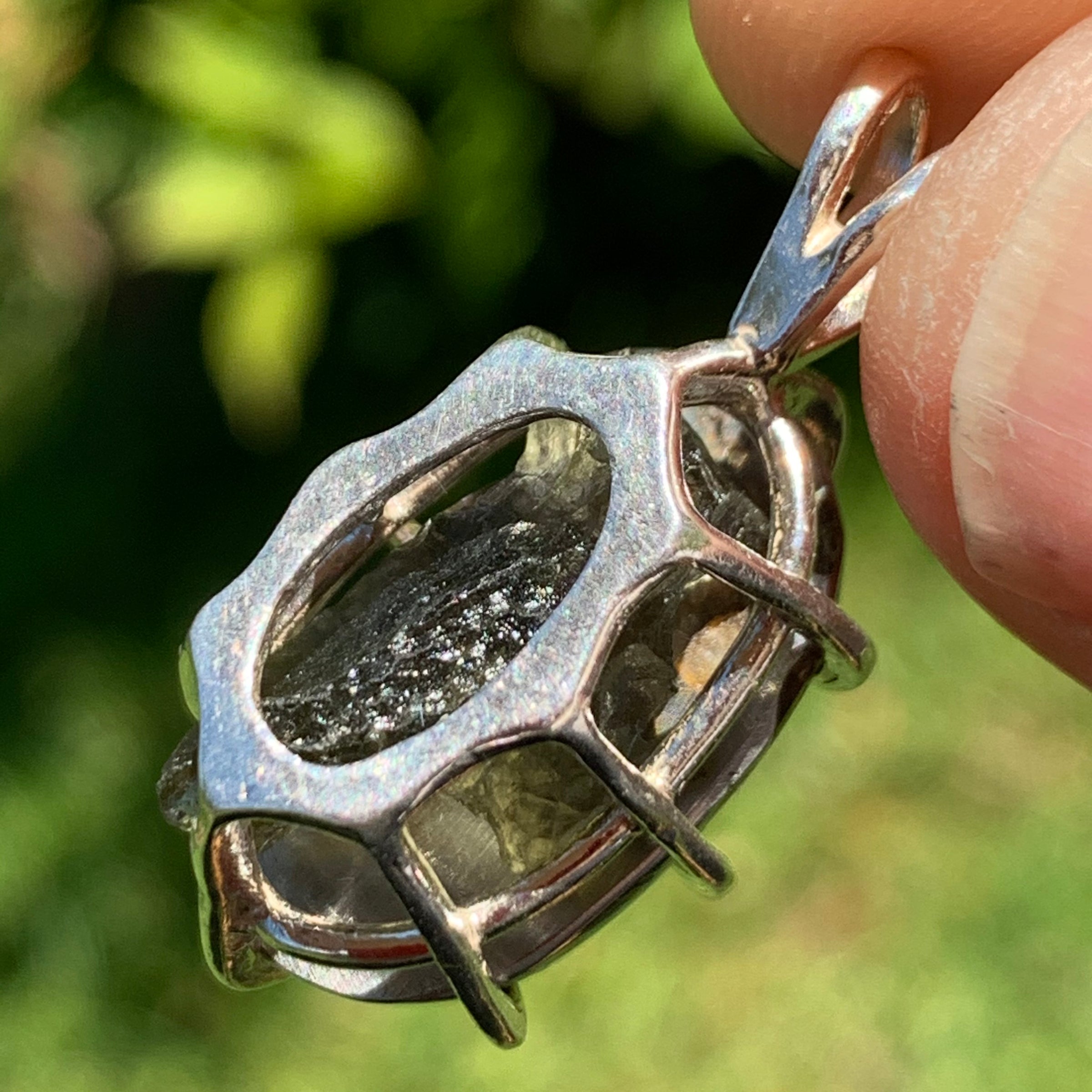 moldavite showing through the backside of a sterling silver sericho pallasite meteorite and raw moldavite tektite basket pendant held up on display to show details