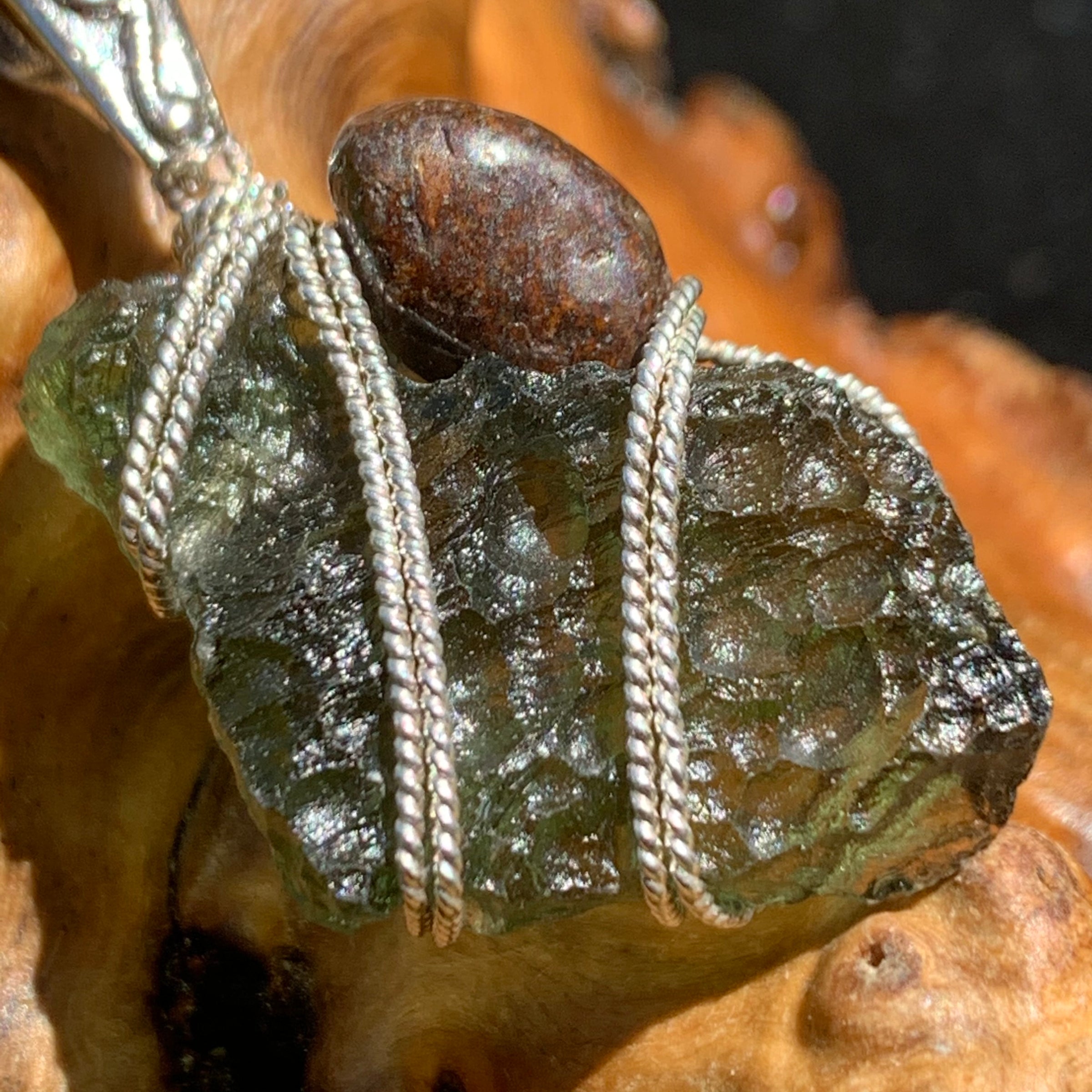 close up of a raw moldavite tektite and nwa 869 meteorite bead sterling silver wire wrapped pendant sitting on driftwood for display
