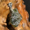 backside of a raw moldavite tektite and nwa 869 meteorite bead sterling silver wire wrapped pendant sitting on driftwood for display