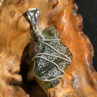 backside of a raw moldavite tektite and nwa 869 meteorite bead sterling silver wire wrapped pendant sitting on driftwood for display