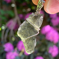 sterling silver wire wrapped raw moldavite tektite pendant up on display with sunlight shining through to show details
