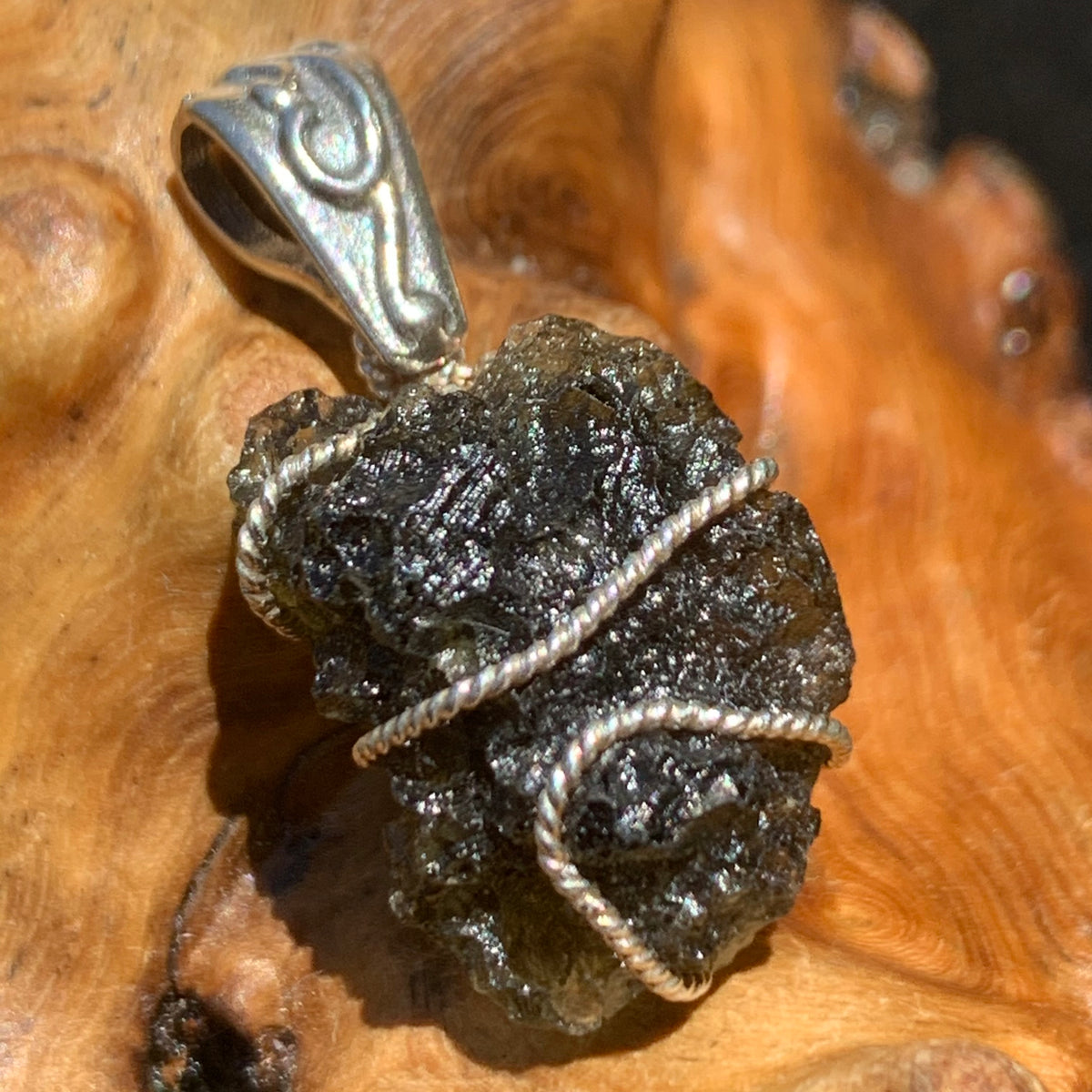 sterling silver wire wrapped raw moldavite tektite pendant sitting on driftwood for display