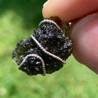 sterling silver wire wrapped raw moldavite tektite pendant held up on display to show details