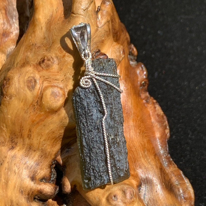sterling silver wire wrapped raw moldavite tektite pendant sitting on driftwood for display