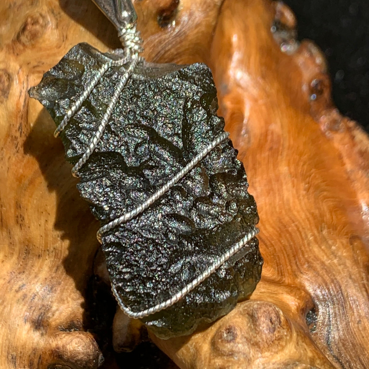 sterling silver wire wrapped raw moldavite tektite pendant sitting on driftwood for display