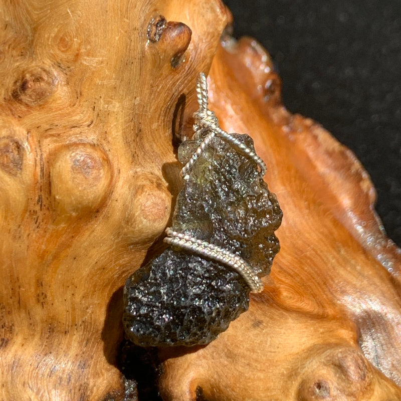 sterling silver wire wrapped raw moldavite tektite pendant sitting on driftwood for display