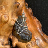 sterling silver wire wrapped raw moldavite tektite pendant sitting on driftwood for display