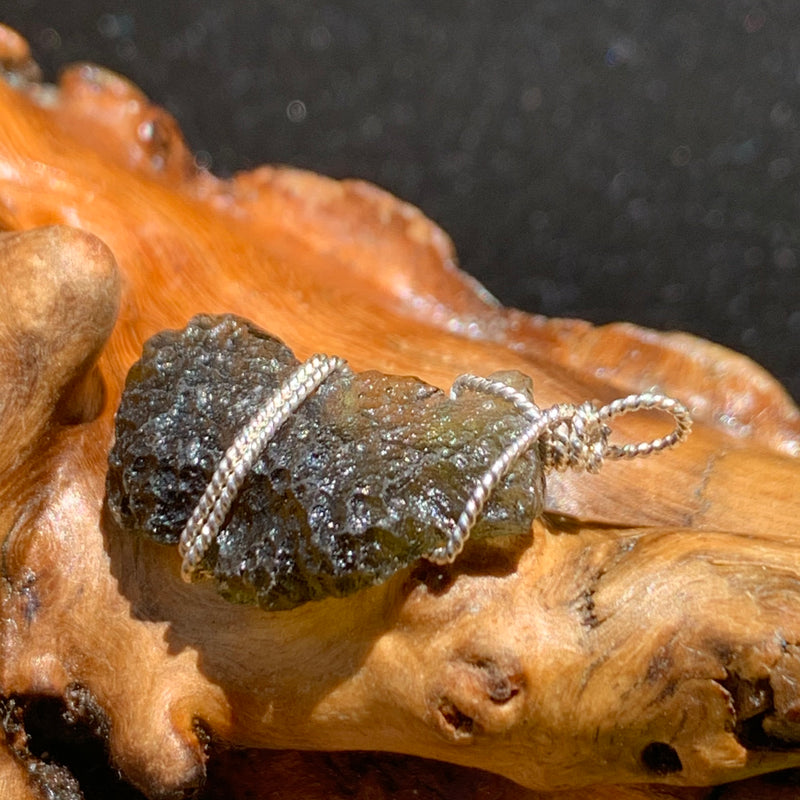 sterling silver wire wrapped raw moldavite tektite pendant sitting on driftwood for display