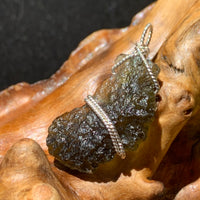 sterling silver wire wrapped raw moldavite tektite pendant sitting on driftwood for display