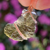 sterling silver wire wrapped raw moldavite tektite pendant up on display with sunlight shining through to show details