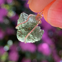 sterling silver wire wrapped raw moldavite tektite pendant up on display with sunlight shining through to show details