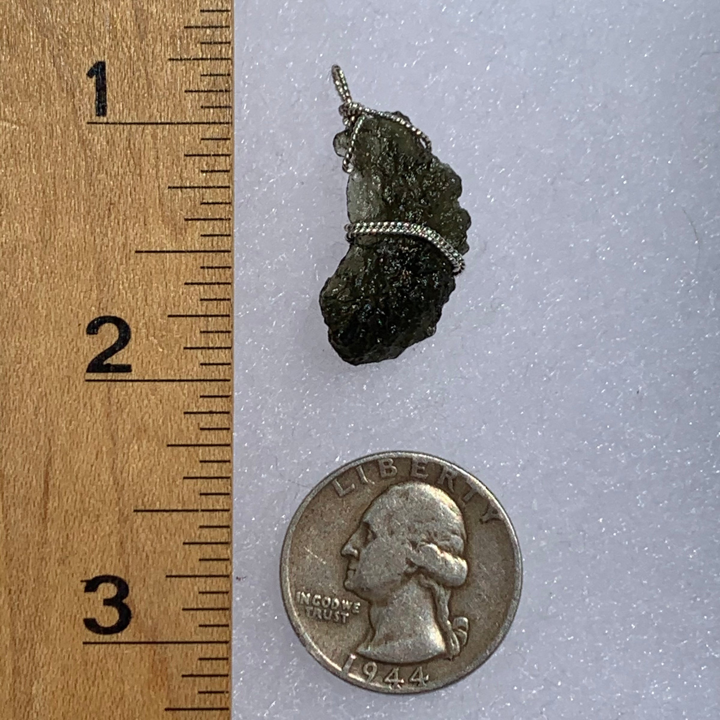 sterling silver wire wrapped raw moldavite tektite pendant next to a ruler and US quarter for scale