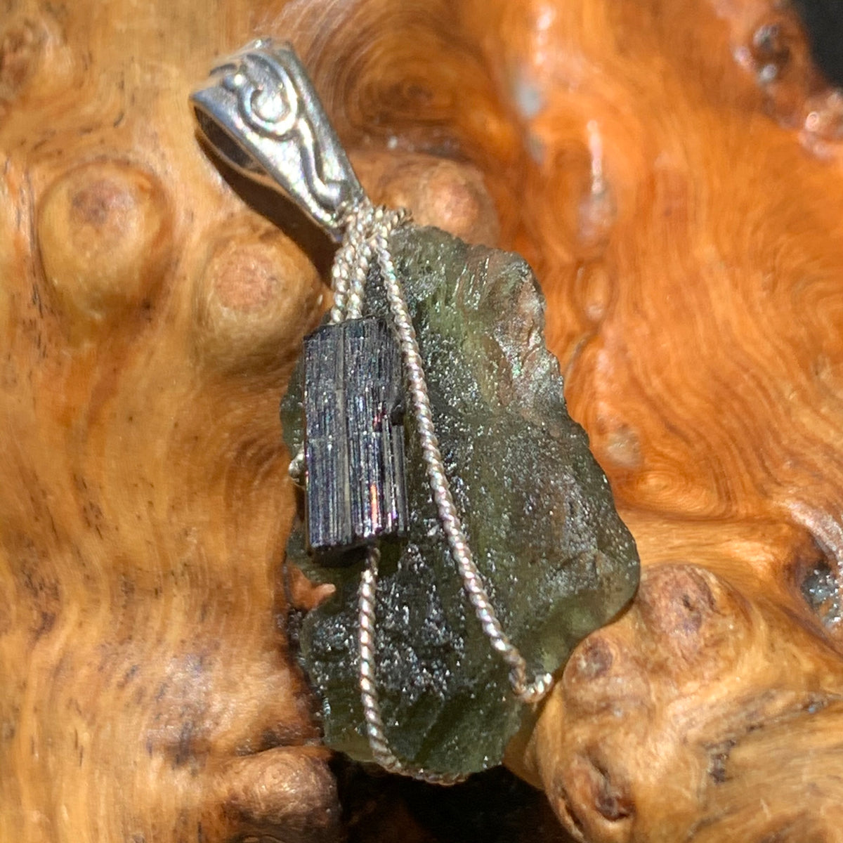 raw moldavite tektite and black tourmaline sterling silver wire wrapped pendant sitting on driftwood for display