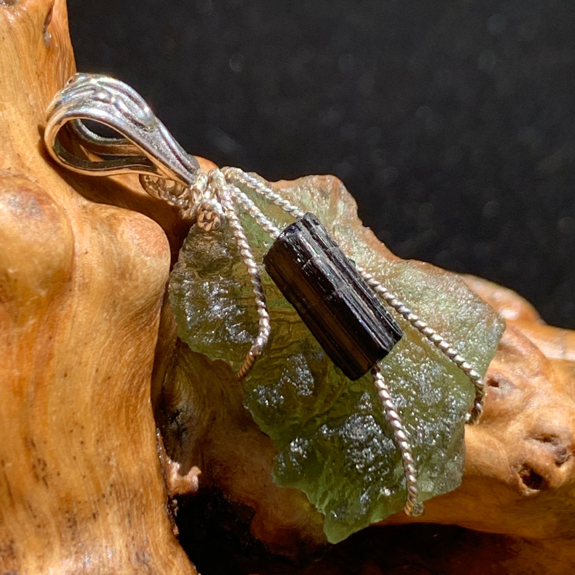 raw moldavite tektite and black tourmaline sterling silver wire wrapped pendant sitting on driftwood for display
