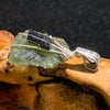 raw moldavite tektite and black tourmaline sterling silver wire wrapped pendant sitting on driftwood for display
