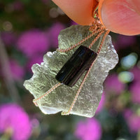 raw moldavite tektite and black tourmaline sterling silver wire wrapped pendant held up on display to show details