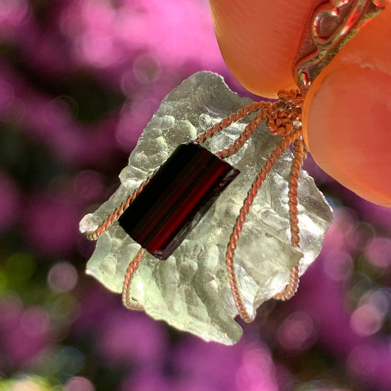 raw moldavite tektite and black tourmaline sterling silver wire wrapped pendant held up on display with sunlight shining through to show details